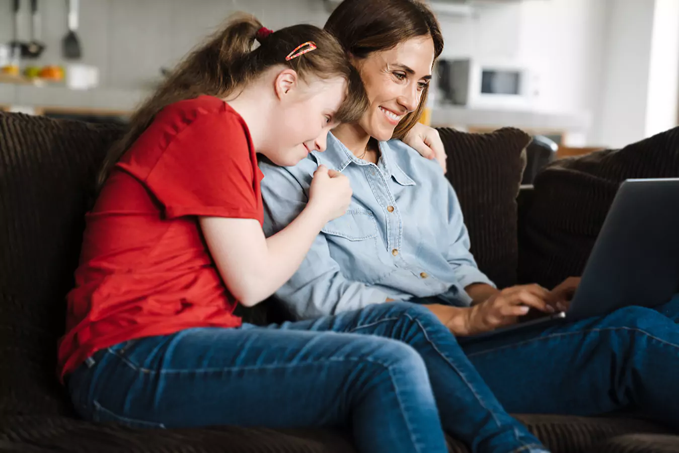 A disabled girl with her support worker smiling while looking at a laptop